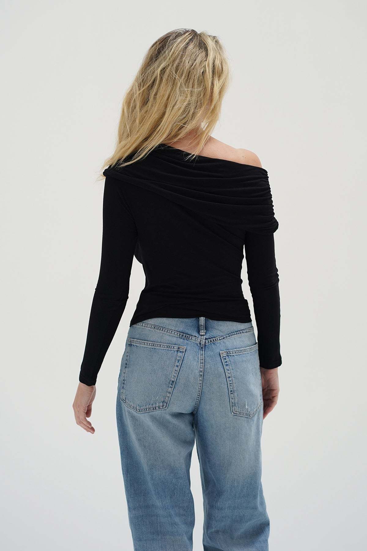 Person wearing a black off-shoulder top and light blue jeans on a white background